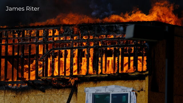 Flames spreading across the exposed wooden framing of a building, photographed by James Riter