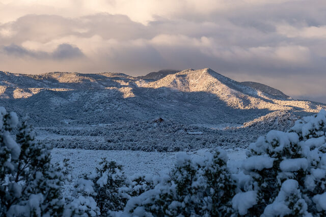 Warm evening light falling across snow-covered hills beneath layered clouds